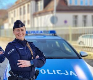 Uśmiechnięta policjantka na tle radiowozu i starówki