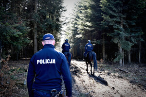 W dukcie leśnym dwaj policjanci na koniach oraz policjant poruszający się pieszo