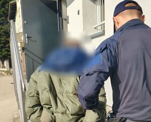 Policjant wprowadzający mężczyznę ze skutymi rękami do siedziby jednostki Policji