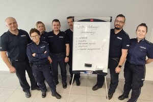 Grupa policjantów i policjantek obok tablicy z odręcznymi wypisami zatytuowanymi "cechy dobrego dzielnicowego"