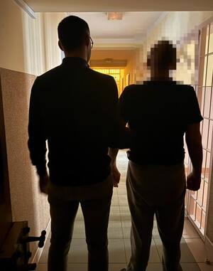 Korytarz przed aresztem widoczni z tyłu policjant i mężczyzna ze zanimizowaną twarzą