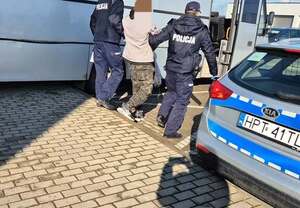 Policjanci doprowadzający mężczyznę z radiowozu do siedziby jednostki