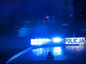 W scenerii nocnej dach radiowozu z galeryjką i włączonymi światłami błyskowymi