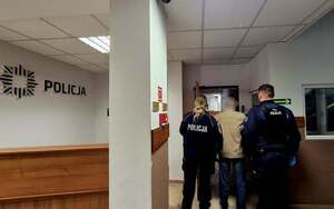 Dwójka policjantów w korytarzu jednostki doprowadzająca mężczyznę