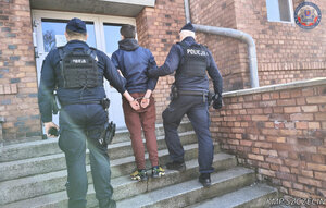 Dwaj Policjanci doprowadzający skutego mężczyznę do jednostki policji