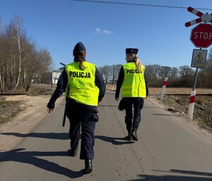 Dwie policjantki w kamizelkach odblaskowych przechodzące przez przejazd kolejowy