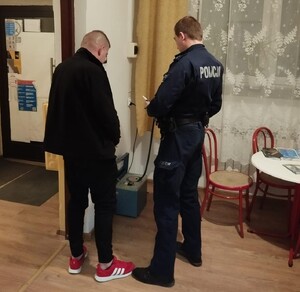 Widziani z tyłu policjant i mężczyzna w czarnej kurtce prowadzący badanie stanu trzeźwości