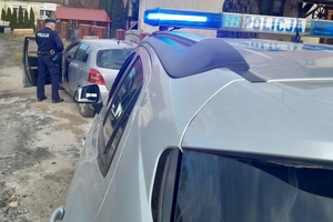 Policjant przy otwartych drzwiach kierowcy samochodu osobowego, na pierwszym tle radiowóz