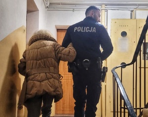 Policjant prowadzący po schodach klatki schodowej bloku seniorkę