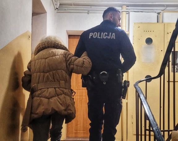 Policjant prowadzący po schodach klatki schodowej bloku seniorkę