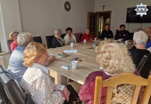 Grupa uśmiechniętych seniorów siedząca przy stole z dwoma policjantami