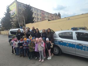 Na tle radiowozu i pojazdu straży miejskiej grupa dzieci, wychowawców oraz policjantów i strażników miejskich