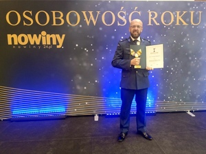 Policjant z dyplomem i statuetką w ręku na tle banneru "Osobowość Roku"