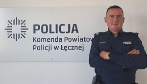 Policjant na tle logo Komendy Powiatowej Policji w Łęcznej