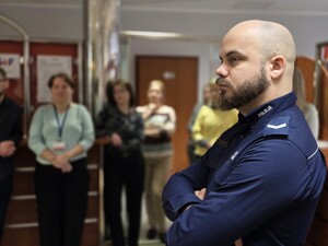 Wewnątrz pomieszczenia policjant, w tle rozmyte sylwetki grupy kobiet
