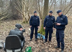 W terenie zadrzewionym trójka policjantów oraz starszy mężczyzna siedzący na starym fotelu
