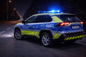 W scenerii nocnej radiowóz stojący na jezdni z włączonymi lampami sygnalizacyjnymi