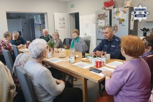 Policjant z grupą seniorów siedzący przy stole w świetlicy