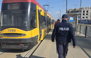 Policjant idący przystankiem tramwajowym, na którym stoi tramwaj