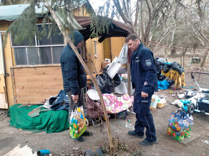 Policjant oraz bezdomny trzymający w rękach świąteczną torbę na tle starej altany ogrodowej