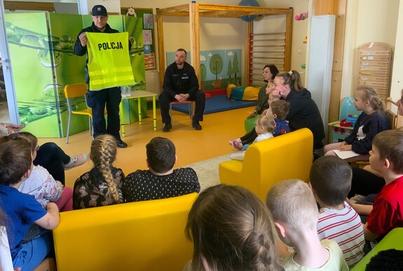 Dwaj policjanci w sali przedszkolnej podczas pogadanki dla dzieci, pokaz policyjnej kamizelki odblaskowej