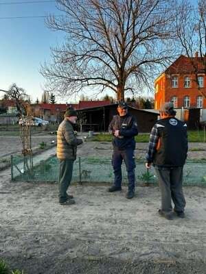Na podwórku w scenerii wiosennej policjant oraz dwóch starszych mężczyzn.