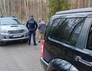 Na leśnej drodze dwa samochody terenowe a między nimi policjant i dwóch mężczyzn