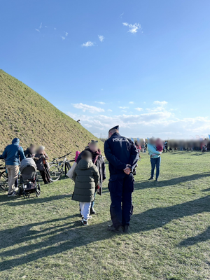 Na tle ściany kopca policjant i grupa ludzi z rowerami