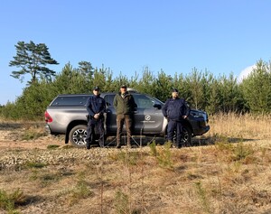 Na tle młodnika i samochodu terenowego dwaj policjanci i strażnik leśny