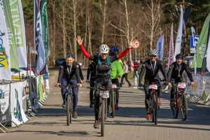 Wśród innych ubranych na sportowo rowerzystów kobieta jadąca rowerem z podniesionymi rękami
