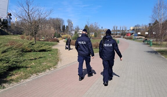 Widziana z tyłu dwójka policjantów idąca chodnikiem przez teren rekreacyjny