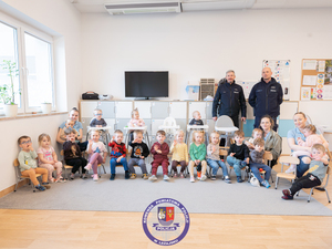 Dwaj policjanci z grupą dzieci pozujących do zdjęcia w sali przedszkolnej