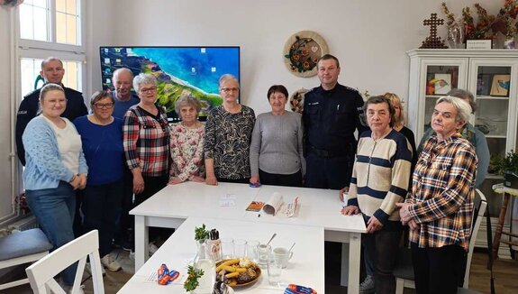 Dwóch policjantów oraz grupa seniorów pozująca do zdjęcia w świetlicy