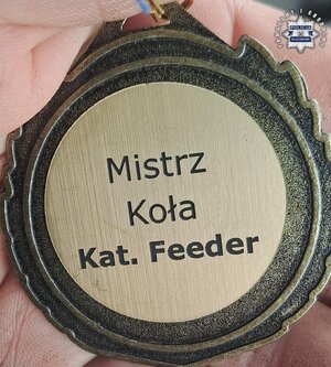 Zbliżenie trzymanego w ręce medalu z napisem Mistrz koła kat. Feeder