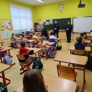 W sali szkolnej dwójka policjantów prowadząca pogadankę dla dzieci siedzących w ławkach