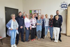 Pozująca do zdjęcia w sali grupa uśmiechniętych seniorek oraz dwóch policjantów