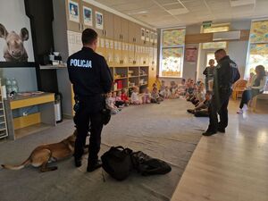 W sali przedszkolnej dzieci siedzące na podłodze oraz dwóch policjantów z psem służbowym