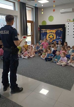 Policjant w trakcie pogadanki dla siedzących na dywanie przedszkolaków
