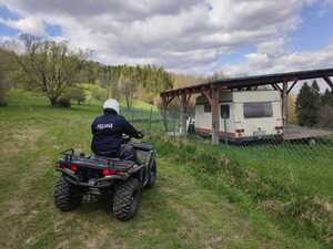 Policjant na quadzie na pochyłej łące obok działki z przyczepą kempingową