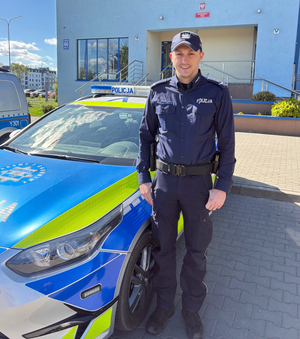 Policjant obok radiowozu na tle siedziby jednostki Policji