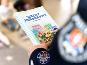 Zbliżenie rąk policjanta trzymających kolorowanki z tytułem Służby mundurowe