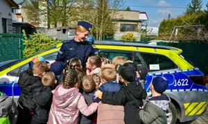 Uśmiechnięta policjantka przed radiowozem otoczona grupką dzieci.