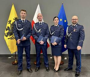 Czwórka policjantów na tle niebieskiej ściany i flag