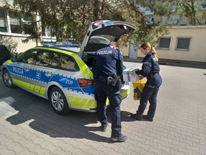 Dwójka policjantów wyjmująca kartony z bagażnika radiowozu.
