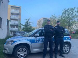 Dwaj policjanci na tle radiowozu stojącego na osiedlu budynków wielorodzinnych