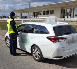 Policjant obok białego samochodu typu kombi na tle peronu kolejowego