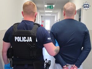 W korytarzu jednostki Policji policjant przytrzymujący mężczyznę ze skutymi z tyłu rękami