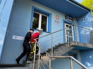 Policjant wprowadzający zatrzymanego mężczyznę po schodach do budynku Policji