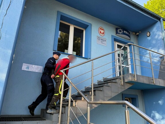 Policjant wprowadzający zatrzymanego mężczyznę po schodach do budynku Policji