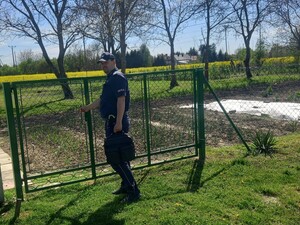 Policjant z teczką przy bramie ogródków działkowych
